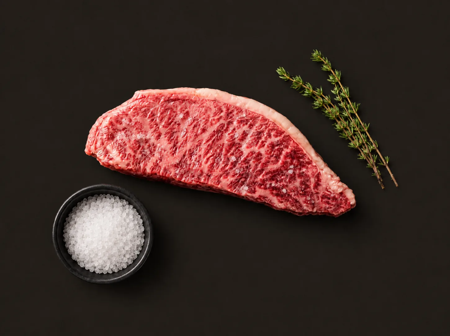 A Kangen Wagyu striploin showing dense marbling, with thyme and sea salt